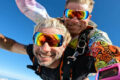 Colorful tandem skydiving pair smile into the camera.