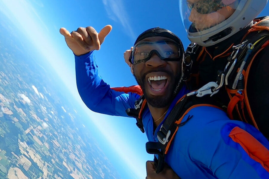 Smiling tandem skydive flashes the hang loose sign.